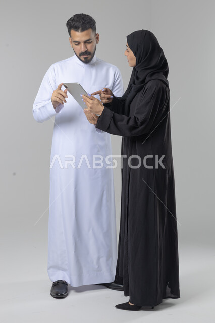 تبادل الأفكار والخبرات لتحقيق أهداف الشركة، العمل الجماعي وروح الفريق الواحد، بورتريه لزميلين عربيين سعوديين خليجيين يقومان بمناقشة و تنظيم الاعمال بإستخدام جهاز التابليت، دمج العمل مع التقنية والتكنولوجيا، صورة الجسم بالطول الكامل، خلفية بيضاء