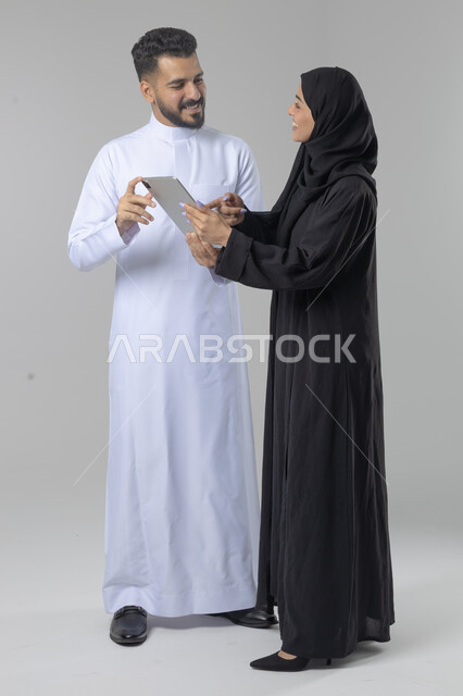 تبادل الأفكار والخبرات لتحقيق أهداف الشركة، العمل الجماعي وروح الفريق الواحد، بورتريه لزميلين عربيين سعوديين خليجيين يقومان بمناقشة و تنظيم الاعمال بإستخدام جهاز التابليت، دمج العمل مع التقنية والتكنولوجيا، صورة الجسم بالطول الكامل، خلفية بيضاء