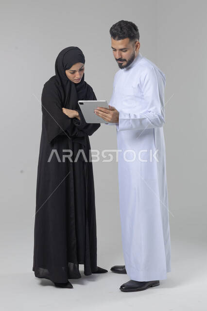 تبادل الأفكار والخبرات لتحقيق أهداف الشركة، العمل الجماعي وروح الفريق الواحد، بورتريه لزميلين عربيين سعوديين خليجيين يقومان بمناقشة و تنظيم الاعمال بإستخدام جهاز التابليت، دمج العمل مع التقنية والتكنولوجيا، صورة الجسم بالطول الكامل، خلفية بيضاء