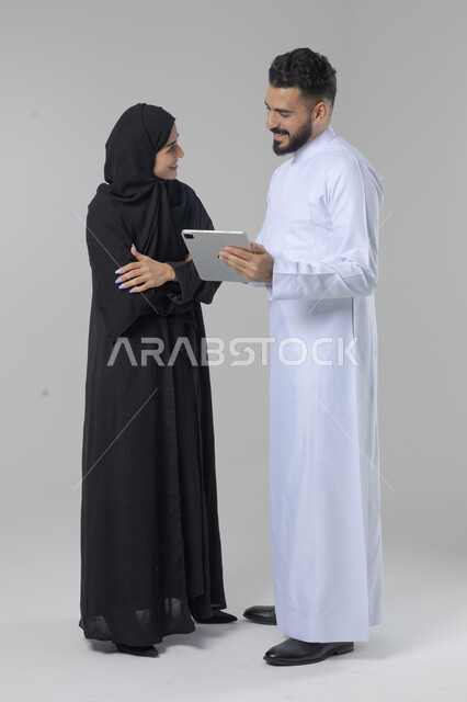 تبادل الأفكار والخبرات لتحقيق أهداف الشركة، العمل الجماعي وروح الفريق الواحد، بورتريه لزميلين عربيين سعوديين خليجيين يقومان بمناقشة و تنظيم الاعمال بإستخدام جهاز التابليت، دمج العمل مع التقنية والتكنولوجيا، صورة الجسم بالطول الكامل، خلفية بيضاء