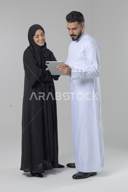 تبادل الأفكار والخبرات لتحقيق أهداف الشركة، العمل الجماعي وروح الفريق الواحد، بورتريه لزميلين عربيين سعوديين خليجيين يقومان بمناقشة و تنظيم الاعمال بإستخدام جهاز التابليت، دمج العمل مع التقنية والتكنولوجيا، صورة الجسم بالطول الكامل، خلفية بيضاء