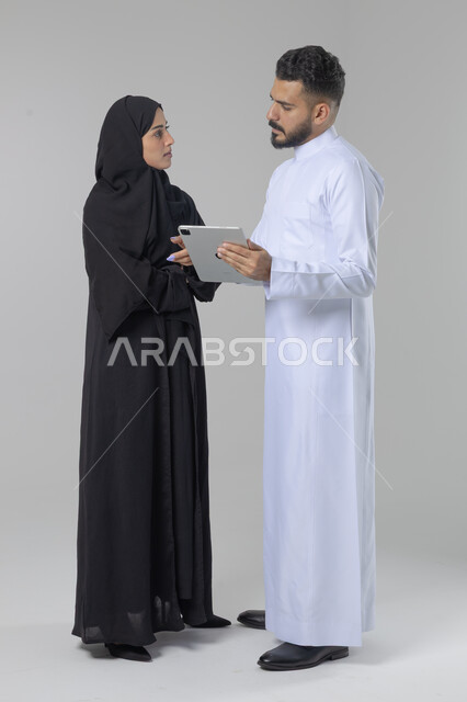 تبادل الأفكار والخبرات لتحقيق أهداف الشركة، العمل الجماعي وروح الفريق الواحد، بورتريه لزميلين عربيين سعوديين خليجيين يقومان بمناقشة و تنظيم الاعمال بإستخدام جهاز التابليت، دمج العمل مع التقنية والتكنولوجيا، صورة الجسم بالطول الكامل، خلفية بيضاء