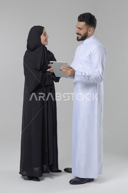 تبادل الأفكار والخبرات لتحقيق أهداف الشركة، العمل الجماعي وروح الفريق الواحد، بورتريه لزميلين عربيين سعوديين خليجيين يقومان بمناقشة و تنظيم الاعمال بإستخدام جهاز التابليت، دمج العمل مع التقنية والتكنولوجيا، صورة الجسم بالطول الكامل، خلفية بيضاء