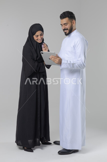 تبادل الأفكار والخبرات لتحقيق أهداف الشركة، العمل الجماعي وروح الفريق الواحد، بورتريه لزميلين عربيين سعوديين خليجيين يقومان بمناقشة و تنظيم الاعمال بإستخدام جهاز التابليت، دمج العمل مع التقنية والتكنولوجيا، صورة الجسم بالطول الكامل، خلفية بيضاء