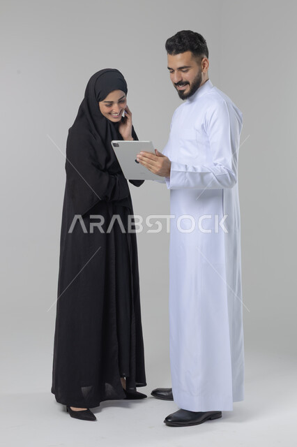 تبادل الأفكار والخبرات لتحقيق أهداف الشركة، العمل الجماعي وروح الفريق الواحد، بورتريه لزميلين عربيين سعوديين خليجيين يقومان بمناقشة و تنظيم الاعمال بإستخدام جهاز التابليت، دمج العمل مع التقنية والتكنولوجيا، صورة الجسم بالطول الكامل، خلفية بيضاء