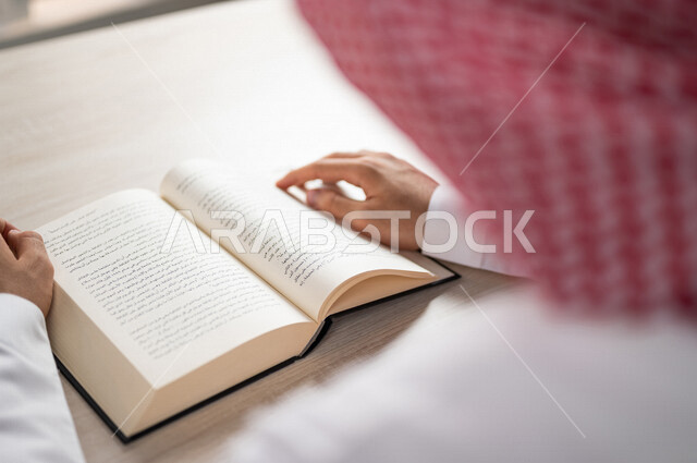 A close-up of a Saudi Arabian Gulf man reading a book, a scientific researcher, a university book, stories and novels, knowledge acquisition, education and culture