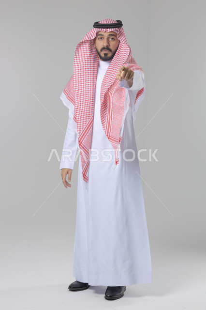 الإشارة إلى شيء ما, الوقوف باستقامة واعتدال, تعابير وايماءات السرور والسعادة، بورتريه لرجل عربي خليجي سعودي يرتدي الثوب التقليدي و الشماغ يشير بيديه لمكان معين, صورة للجسم بالطول الكامل, خلفية بيضاء