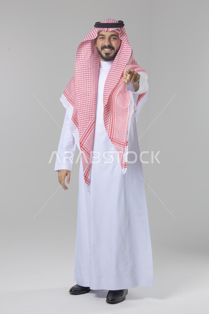 الإشارة إلى شيء ما, الوقوف باستقامة واعتدال, تعابير وايماءات السرور والسعادة، بورتريه لرجل عربي خليجي سعودي يرتدي الثوب التقليدي و الشماغ يشير بيديه لمكان معين, صورة للجسم بالطول الكامل, خلفية بيضاء