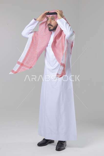 الاهتمام بالمظهر الخارجي و الشياكه و الأناقة, بورتريه لشاب سعودي عربي خليجي يرتدي الثوب والشماغ الأحمر يقوم بالتزين و التجمل و الترتيب, الاستعداد للخروج والذهاب، خطوات لبس الشماغ السعودي التقليدي, الجسم بالطول الكامل، خلفية بيضاء