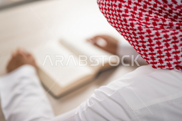 A close-up of a Saudi Arabian Gulf man reading a book, a scientific researcher, a university book, stories and novels, knowledge acquisition, education and culture