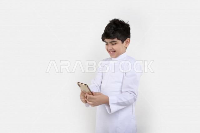 بورتريه لفتى عربي خليجي سعودي مبتسم بيده هاتف محمول ، تسويق إلكتروني ، إستخدام التطبيقات الالكترونية ، ألعاب فيديو ، التعلم عن بعد ، التسوق و الشراء ، خلفية بيضاء