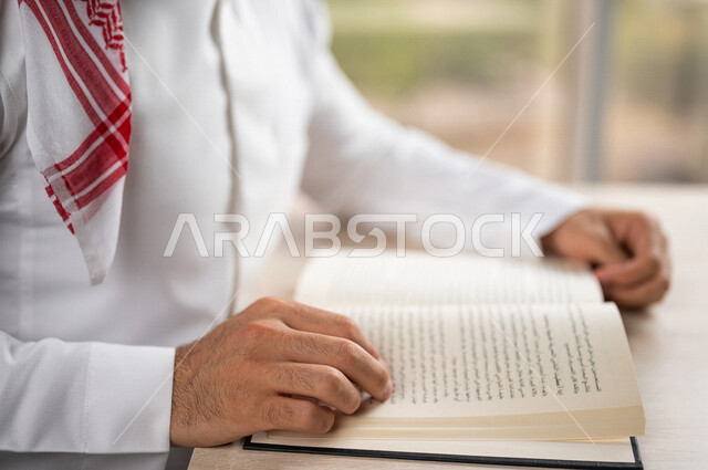 A close-up of a Saudi Arabian Gulf man reading a book, a scientific researcher, a university book, stories and novels, knowledge acquisition, education and culture