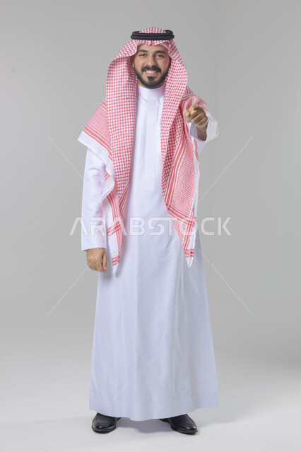 الإشارة إلى شيء ما, الوقوف باستقامة واعتدال, بورتريه لرجل عربي خليجي سعودي يرتدي الثوب التقليدي و الشماغ يشير بيديه لمكان معين, صورة للجسم بالطول الكامل, خلفية بيضاء