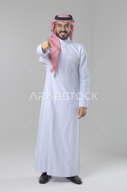 الإشارة إلى شيء ما, الوقوف باستقامة واعتدال, بورتريه لرجل عربي خليجي سعودي يرتدي الثوب التقليدي و الشماغ يشير بيديه لمكان معين, صورة للجسم بالطول الكامل, خلفية بيضاء