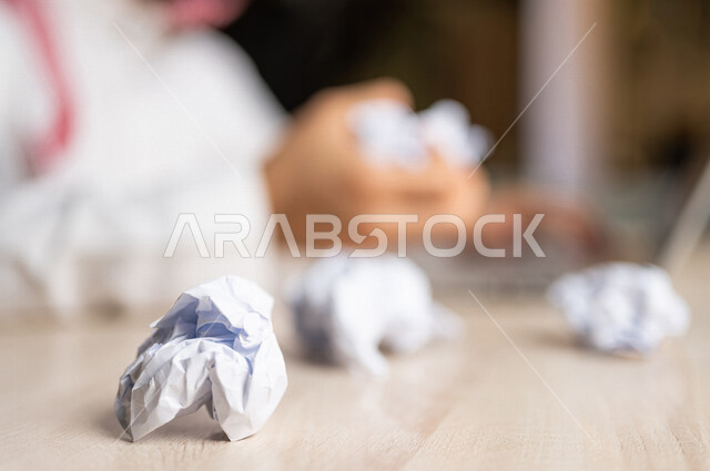رجل عربي خليجي سعودي يجلس امام الحاسوب المحمول، القيام بتجعيد الأوراق، البحث عن افكار وخطط، الاخفاق في الكتابة والتدوين، الفشل في الابداع والعمل، محاولة ايجاد حلول