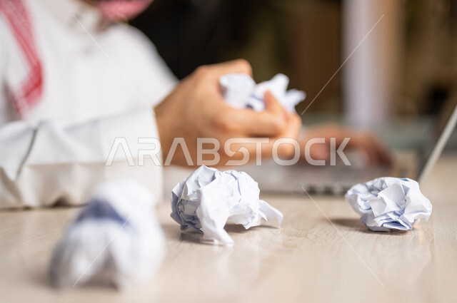رجل عربي خليجي سعودي يجلس امام الحاسوب المحمول، القيام بتجعيد الأوراق، البحث عن افكار وخطط، الاخفاق في الكتابة والتدوين، الفشل في الابداع والعمل، محاولة ايجاد حلول
