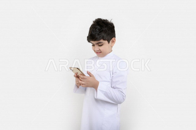 بورتريه لفتى عربي خليجي سعودي مبتسم بيده هاتف محمول ، تسويق إلكتروني ، إستخدام التطبيقات الالكترونية ، ألعاب فيديو ، التعلم عن بعد ، التسوق و الشراء ، خلفية بيضاء