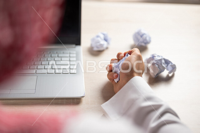 A Saudi Arabian Gulf man sitting in front of a laptop, creasing papers, searching for ideas and plans, failing to write and blogging, failing to be creative and working, trying to find solutions
