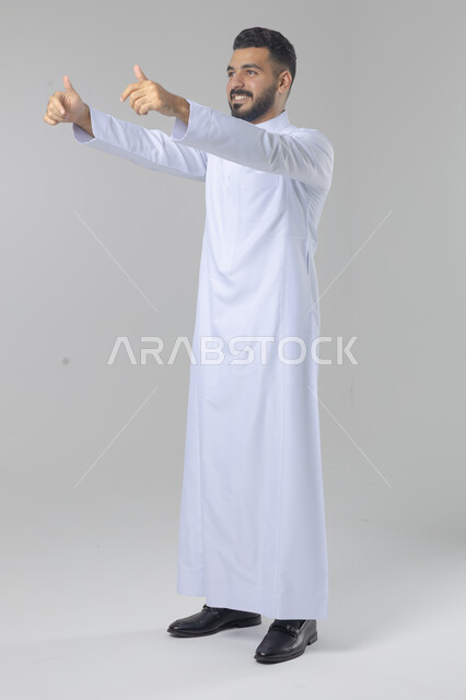  الإمتياز والتميز والنجاح، بورتريه لرجل عربي خليجي سعودي يرتدي الثوب التقليدي ويرفع أصابع الإبهام لأعلى، إيماءات السعادة والإعجاب والموافقة، حركة أصبع تدل على القبول والرضا، الجسم بالطول الكامل، خلفية بيضاء 