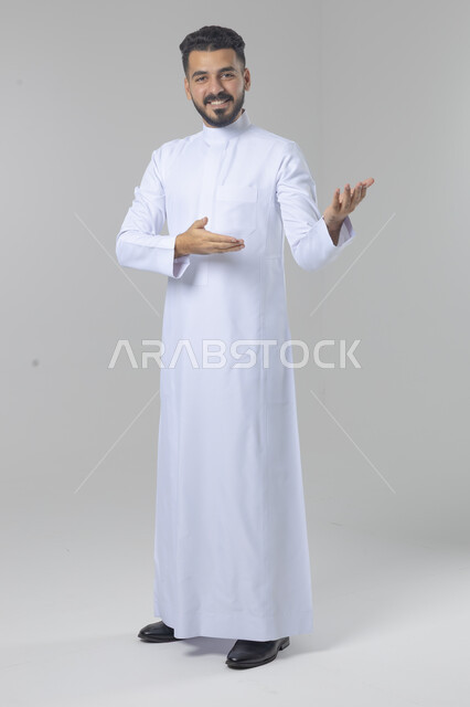 الإشارة إلى شيء ما, الوقوف باستقامة واعتدال, بورتريه لرجل عربي خليجي سعودي يرتدي الثوب التقليدي يشير بيديه لمكان معين, صورة للجسم بالطول الكامل, خلفية بيضاء