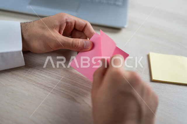 صورة مقربة لرجل عربي خليجي سعودي، الكتابة على اوراق  صغيرة، أوراق قرطاسية صغيرة، كتابة المهام، مجموعة من الورق الملون، أعمال مكتبية