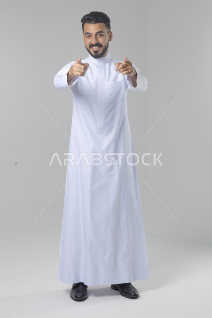 الإشارة إلى شيء ما, الوقوف باستقامة واعتدال, بورتريه لرجل عربي خليجي سعودي يرتدي الثوب التقليدي يشير بيديه لمكان معين, صورة للجسم بالطول الكامل, خلفية بيضاء