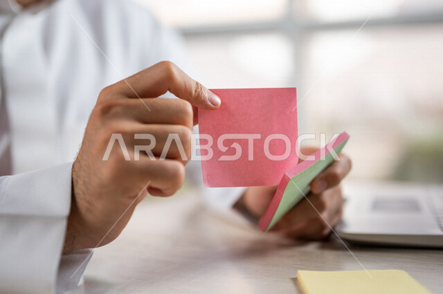 صورة مقربة لرجل عربي خليجي سعودي، الكتابة على اوراق  صغيرة، أوراق قرطاسية صغيرة، كتابة المهام، مجموعة من الورق الملون، أعمال مكتبية