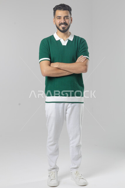  التقاط صور شخصية للوثائق الرسمية، الاعتناء والاهتمام بالمظهر الخارجي، مفهوم الاناقة والرجولة، بورتريه لشاب عربي خليجي سعودي يرتدي الزي الكاجوال يقف بأيدي متقاطعة ينظر الى الكاميرا بتعابير السرور والثقة بالنفس، الجسم بالطول الكامل، خلفية بيضاء