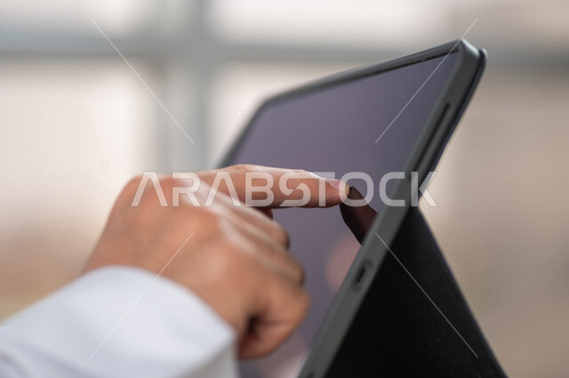 صورة مقربة ليد رجل عربي خليجي سعودي ينقر على شاشة جهاز التابلت، شرح خطوات العمل، دورات الكترونية، التسويق الالكتروني، تصفح المواقع الالكترونية، القيام بالاعمال الادارية