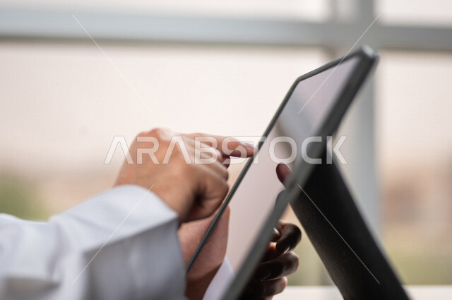 صورة مقربة ليد رجل عربي خليجي سعودي ينقر على شاشة جهاز التابلت، شرح خطوات العمل، دورات الكترونية، التسويق الالكتروني، تصفح المواقع الالكترونية، القيام بالاعمال الادارية