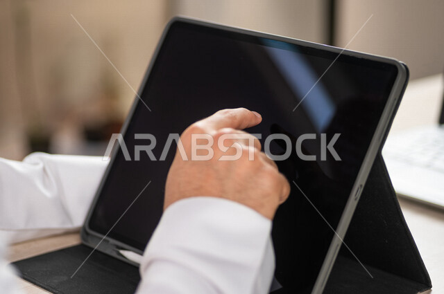 صورة مقربة ليد رجل عربي خليجي سعودي ينقر على شاشة جهاز التابلت، شرح خطوات العمل، دورات الكترونية، التسويق الالكتروني، تصفح المواقع الالكترونية، القيام بالاعمال الادارية