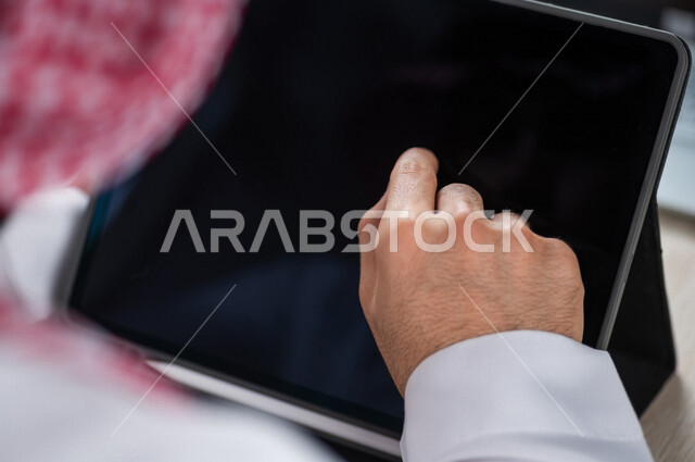 صورة مقربة ليد رجل عربي خليجي سعودي ينقر على شاشة جهاز التابلت، شرح خطوات العمل، دورات الكترونية، التسويق الالكتروني، تصفح المواقع الالكترونية، القيام بالاعمال الادارية