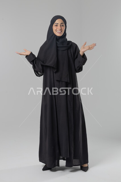  التوضيح والدلالة لمكان محدد, الإشارة إلى عنصر ما, بورتريه لامرأة عربية خليجية سعودية محجبة ترتدي العباءة تشير بيديها على الجانب، تحديد موقع شيء معين, صورة الجسم بالطول الكامل، خلفية بيضاء
