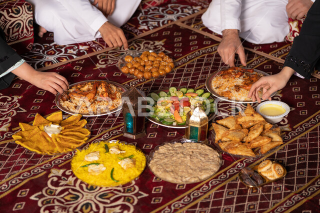 المأكولات العربية الشرقية, زينة وأضواء وفوانيس الاحتفال بقدوم شهر الخير, سفرة مليئة بالأصناف والمقبلات الشهية, صورة مقربة ليد عائله عربيه خليجيه اماراتية يقومون بتناول الافطار وقت اذان المغرب ،  إفطار رمضاني عائلي