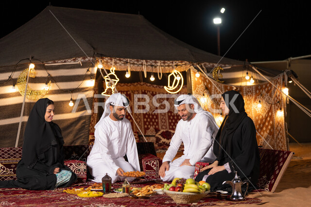 تبادل الأحاديث بين أفراد الأسرة، أداء فريضة الصيام في شهر رمضان المبارك، سفرة مليئة بأصناف من المأكولات الشرقية الشهية، أجواء عائلية دينية رمضانية سعيدة، عائلة عربية خليجية اماراتية مجتمعة حول مائدة الطعام، زينة المناسبات الإسلامية، التخييم في الصحراء
