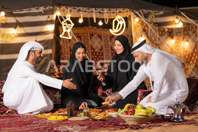 التخييم في الصحراء وقت الافطار, مائدة إفطار مليئة بأصناف المأكولات الشهية، مفهوم الضيافة العربية وحسن استقبال الضيوف، عائلة عربية خليجية اماراتيه يرتدون الثوب التقليدي يتناولون الافطار, أجواء شهر رمضان المبارك , أصناف متنوعة من المأكولات
