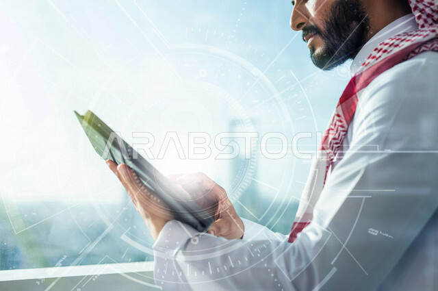 رجل اعمال عربي سعودي خليجي يستخدم جهاز تفني لمتابعة الأعمال المكتبيه, رسومات هولوجراميه توضح نسبة انجاز الاعمال, متابعة سوق الاسهم, الاقتصاد المالي, اعمال الكترونيه تجاريه, حسابات واحصاءات بيانيه باستخدام تقنية الهولوجرام ثلاثية الابعاد