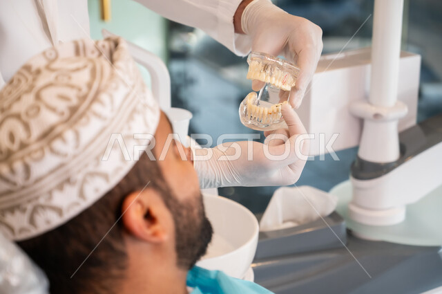 Using the necessary tools and equipment, providing advice for maintaining oral and dental health, taking care of oral health, the concept of medicine and health care, a close-up side view of an Arab Gulf Omani man wearing a mask sitting on a treatment chair in a dental clinic