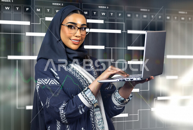 إمرأه عربيه سعوديه خليجيه تؤدي أعمالها عبر جهاز الحاسوب, متابعة وتخطيط المهام اليوميه, رسم جداول الاعمال بتقنية الهولوجرام, انجاز الاعمال في مقر العمل , تحقيق اهداف الشركه, تطوير العمل, بيئة العمل السعودي