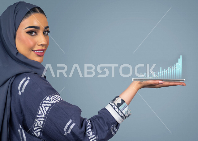 إمرأه عربيه سعوديه خليجيه  تحمل بيدها رسومات هولوجراميه ثلاثية الابعاد, مخطط بياني للإقتصاد المالي، تحليل البيانات ورسمها بتقنية الهولوجرام، تخطيط وتحليل البيانات و المعلومات