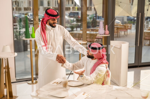 مفهوم الاستقبال والترحيب، إيماءات السرور والسعادة برؤية الأصدقاء، إلقاء التحيه والسلام, رجلان عربيان خليجيان سعوديان يتقابلان في المقهى ويقومان بمصافحة بعضهما, صداقة وتعارف وبناء علاقات اجتماعية، قضاء وقت ممتع في الخارج