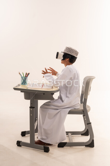 Integrating modern technologies into scientific life, simulating the virtual world, a side portrait of an Arab Gulf Omani student wearing a dishdasha, a kummah, and 3D virtual reality glasses, sitting at an office table playing with gestures and hand expressions indicating integration, white background