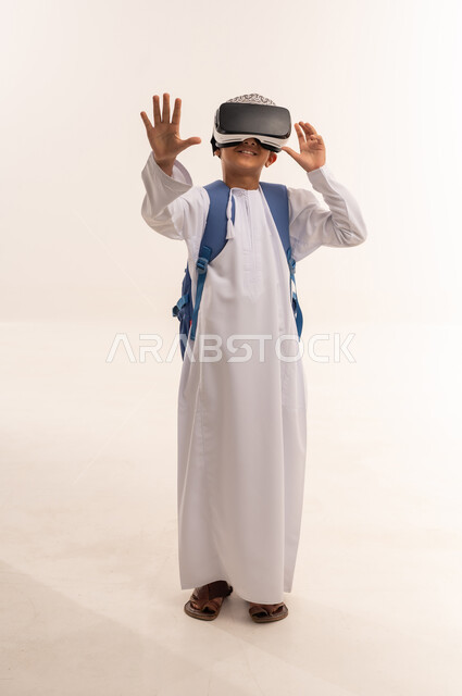 التفاعل والاندماج ومحاكاة العالم الخيالي، بورترية لطالب عربي خليجي عماني يرتدي الدشداشة و الكمة يضع حقيبة الظهر المدرسية يقوم بمشاهدة الافلام ثلاثية الابعاد, قضاء أوقات الفراغ بالأنشطة الالكترونية المسلية, الجسم بالطول الكامل, خلفية بيضاء