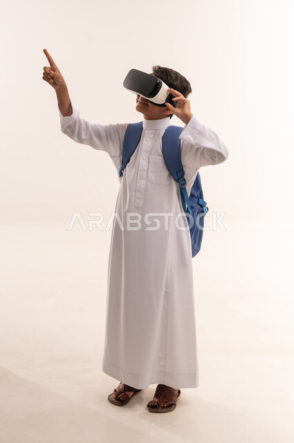 مفهوم التقنيات الإلكترونية الحديثة، بورترية لطالب عربي خليجي عماني يرتدي الزي التقليدي  يضع حقيبة الظهر المدرسية، ولد سعودي يقوم بمشاهدة الافلام ثلاثية الابعاد, قضاء أوقات الفراغ بالأنشطة الالكترونية المسلية, الجسم بالطول الكامل, خلفية بيضاء