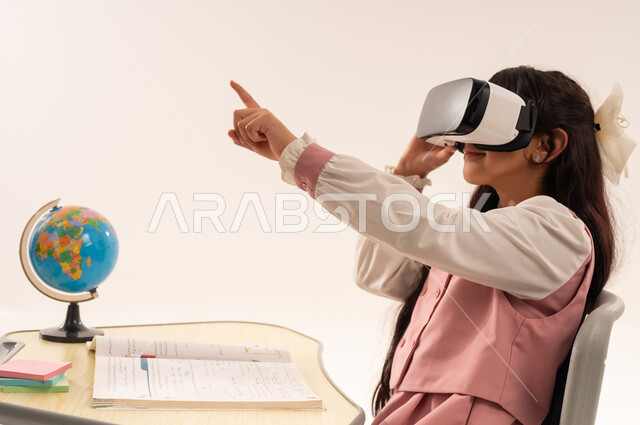 Integrating modern technologies into academic life, following new educational methods, a Saudi female student sitting at a study table and pointing at something, a close-up side portrait of an Arab Gulf Omani female student wearing a school uniform enjoying watching through virtual reality glasses, white background