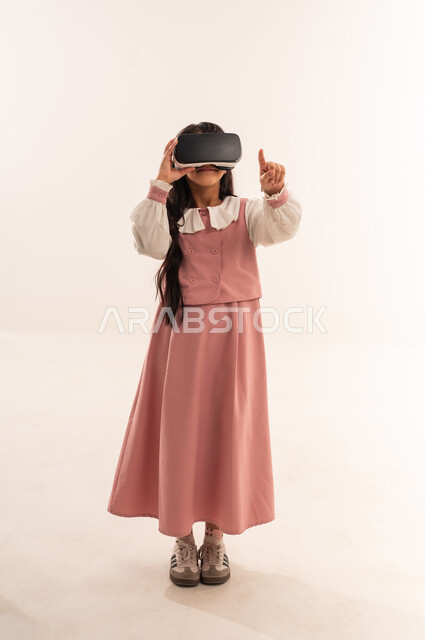 جمع التعلم مع الترفيه بإستخدام التقنيه والتكنولوجيا الحديثه, التعليم الذكي عبر نظارات الواقع الافتراضي, مدارس وأكاديميات متطوره، بورتريه لتلميذة عربية خليجية  عمانية ترتدي اليونيفورم والحقيبة المدرسية، طالبه سعودية تشير إلى شيء ما, الجسم بالطول الكامل، خلفية بيضاء
