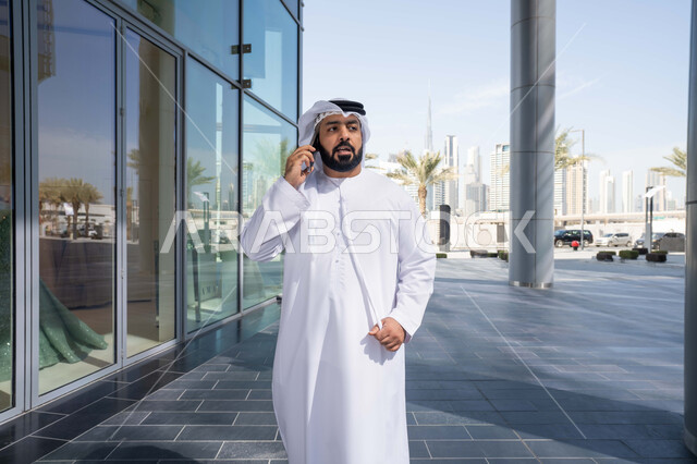 ايماءات السعادة والسرور، استخدام التكنولوجيا والتقنيات الحديثه، نزهة وجولة فى الهواء الطلق ، برامج وتطبيقات الانترنت ، الدردشة مع الاصدقاء ، توثيق اللحظات السعيدة، رجل عربي خليجي اماراتي يرتدي الكندورة والغترة البيضاء، ينظر بتعابير السرور يقوم باستخدام الهاتف المحمول ، التسوق عبر تطبيقات الاونلاين .