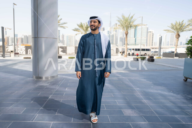 قضاء اوقات ممتعة فى الطبيعة ، الفخر والاعتزاز بالتقدم المعماري ، التجول واستنشاق الهواء النقي في الخارج, النمو العمراني في المدينة ، قضاء وقت ممتع ف الامارات ، رجل عربي خليجي اماراتي يرتدي الكندورة والغترة البيضاء ينظر الى شيء ما في وقت النهار .