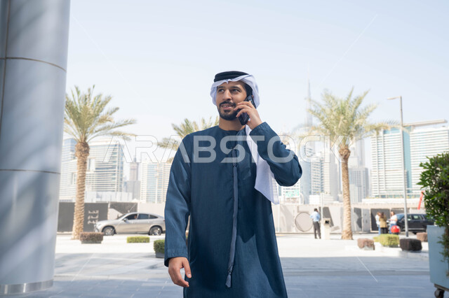 التواصل مع العائلة عبر الجوال ، استخدام التكنولوجيا والتقنيات الحديثه، نزهة وجولة فى الهواء الطلق ، برامج وتطبيقات الانترنت ، الدردشة مع الاصدقاء ، توثيق اللحظات السعيدة، رجل عربي خليجي اماراتي يرتدي الكندورة والغترة البيضاء، ينظر بتعابير السرور يقوم باستخدام الهاتف المحمول ، التسوق عبر تطبيقات الاونلاين  .