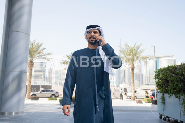 ايماءات السعادة والسرور، استخدام التكنولوجيا والتقنيات الحديثه، نزهة وجولة فى الهواء الطلق ، برامج وتطبيقات الانترنت ، الدردشة مع الاصدقاء ، توثيق اللحظات السعيدة، رجل عربي خليجي اماراتي يرتدي الكندورة والغترة البيضاء، ينظر بتعابير السرور يقوم باستخدام الهاتف المحمول ، التسوق عبر تطبيقات الاونلاين  .